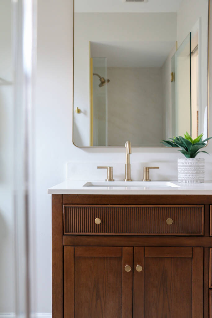 Bathroom remodel showing a dark wood vanity with gold mirror and hardware