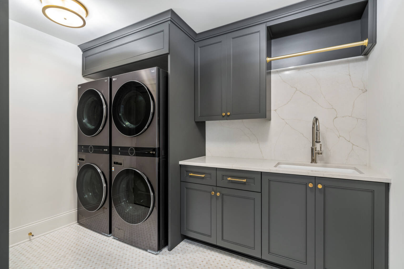 Luxury laundry room design featuring dark cabinets and double washer and dryer appliance.